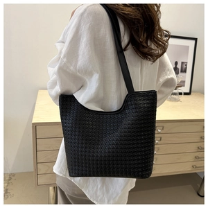 Close-up of black woven leather tote bag showing detailed square grid texture and slim handles