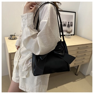 Gros plan d'un sac cabas noir brillant avec un grand nœud décoratif et deux anses