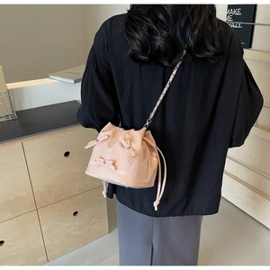 Détail du sac seau en cuir verni rose avec nœuds et bandoulière chaîne porté par le modèle