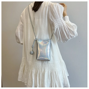 Detail showing holograph silver mini crossbody bag and woven ball pendant on white dress