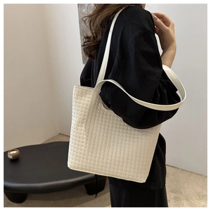 Detail of cream woven tote bag showing fine texture and long shoulder strap on model