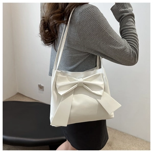Détail d'un sac à bandoulière beige avec grand nœud porté par un mannequin femme