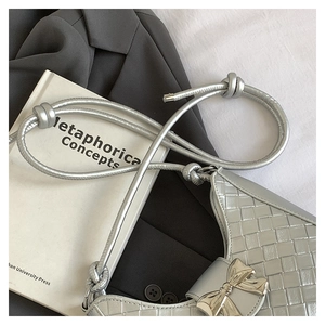 Macro detail of silver woven handbag with metallic bow clasp and thin knot strap
