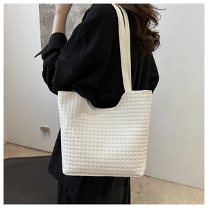 Detail shot of cream woven tote bag showing the texture and strap on a model's shoulder