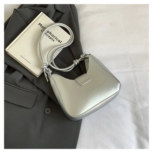 Close-up of silver metallic shoulder bag featuring a unique knotted strap design and sleek finish