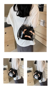 Détail du sac seau en cuir verni noir avec nœuds roses et bandoulière chaîne