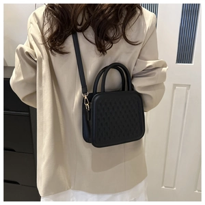 Detail of black textured crossbody bag with gold hardware and embossed patterns