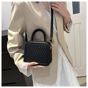 Close-up of black quilted small square bag with top handle and adjustable gold buckle strap