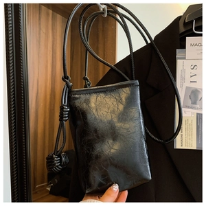 Detail of minimalist black crossbody phone bag with wax-feel texture and knotted strap