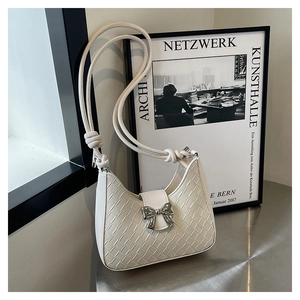 Detail of white woven hobo bag featuring a silver metal bow and knotted shoulder strap