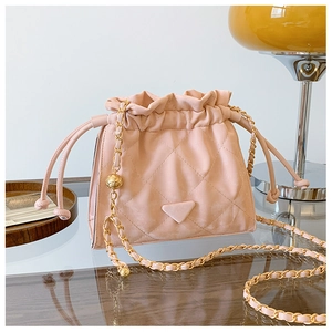 Détail du sac seau matelassé rose avec bandoulière chaîne dorée sur table en verre