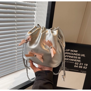 Détail du sac seau argenté avec nœuds roses et bandoulière chaîne tenu à la main