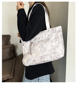 Close-up of white canvas tote bag with grey teddy bear print and small round charm