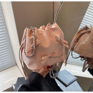 Sac seau rose brillant avec nœud et chaîne argentée présenté dans un reflet de miroir