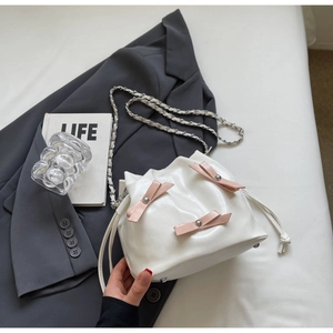 Détail du sac seau plissé blanc avec nœuds en cuir rose et bandoulière en chaîne argentée