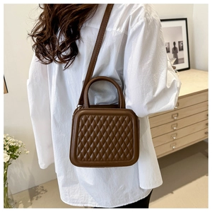 Detail of dark brown quilted crossbody bag with top handle worn over a model shoulder