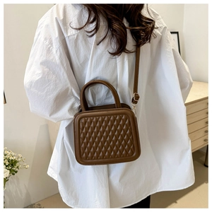 Detailed view of a brown quilted crossbody bag worn by a model in a white shirt