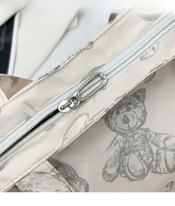Detail of silver smooth metal zipper and gray bear print on creamy white tote bag