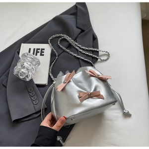 Détail du sac seau argenté avec nœuds en cuir rose et bandoulière chaîne sur un blazer