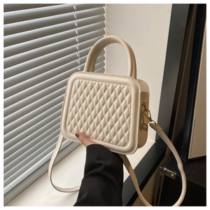 Close-up of cream quilted square handbag with gold hardware and stylish handle