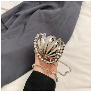 Detail view of silver shell-shaped metallic crossbody bag with beaded handle and chain
