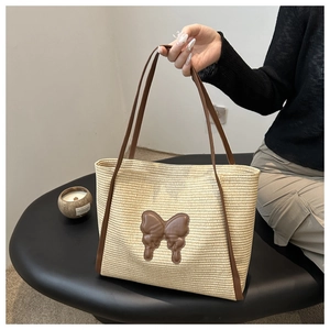 Detail of woven straw tote bag featuring a leather butterfly motif and long shoulder straps