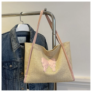 Detail of straw tote bag featuring pink leather trim and decorative butterfly applique