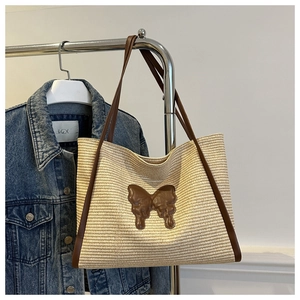 Detail of a straw tote bag with brown butterfly patch and leather straps on denim background