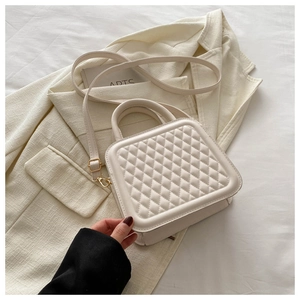 Detailed shot of white quilted square bag with gold hardware on beige blazer background