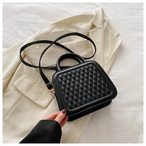 Detail of black quilted crossbody bag with matte texture and gold hardware on blazer
