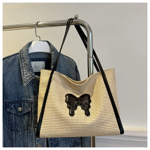 Detail of summer straw tote bag with black leather butterfly patch and shoulder straps