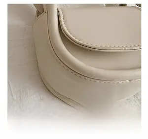 Detail showing precise stitching on beige leather surface of a minimalist crossbody bag