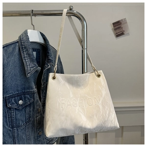 Detail view of white wrinkled texture shoulder bag with gold metal rings on a hanger