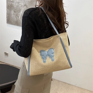 Straw tote bag with blue butterfly detail and shoulder straps shown on a model
