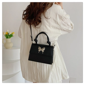 Détail du sac carré noir avec papillon argenté sur une chemise blanche plissée chic