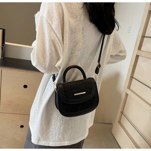 Detail of a black leather saddle bag featuring a sleek gold metal buckle and textured finish