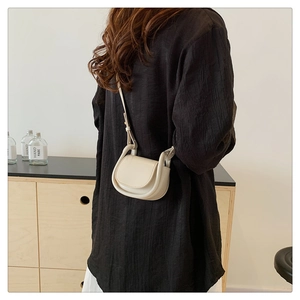Close-up of minimalist beige crossbody bag showing sleek curves and matte leather texture