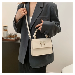 Détail du sac carré crème minimaliste avec boucle papillon en métal et poignée à nœud élégante