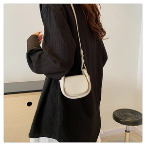 Model wearing a cream leather saddle bag with a minimalist design and slim shoulder strap