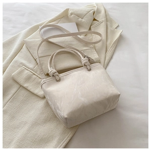 Détail du sac à main blanc à motif marbre avec nœuds sur une veste de costume beige