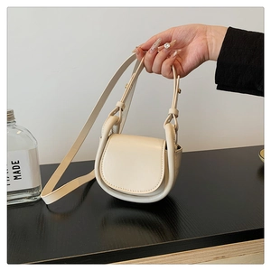 Detail of a creamy white saddle bag with adjustable strap and flap closure