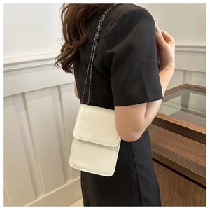 Side view of a woman wearing a cream leather mini crossbody phone bag with metal chain