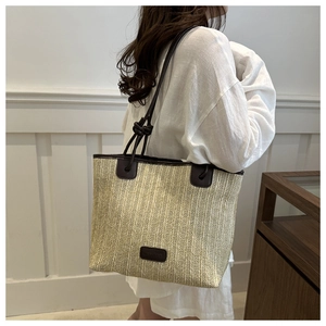 Detail view of woven straw tote bag with brown leather handles and brand patch