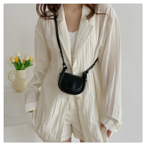 Minimalist black leather mini crossbody bag worn as a stylish accessory on a white suit
