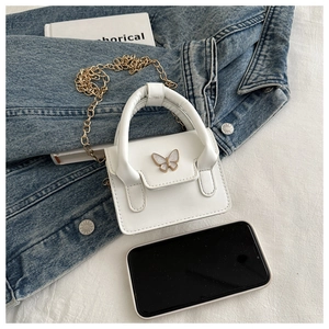 Mini white crossbody bag with gold butterfly hardware and chain strap next to a phone