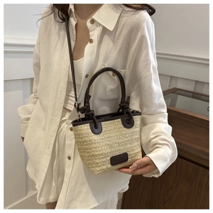 Detail view of woven straw tote bag featuring brown leather handles and adjustable strap