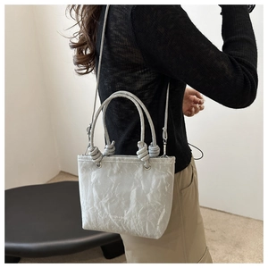 Détail du sac seau gris montrant la texture plissée et la poignée décorative nouée