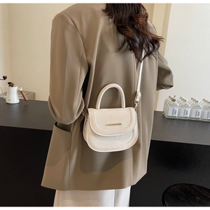 Detail of a minimalist cream-colored crossbody saddle bag with sleek metal bar hardware