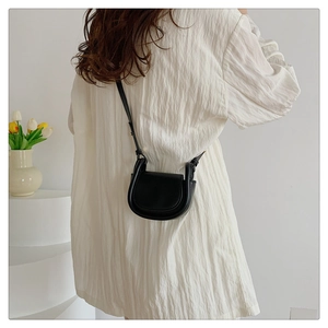 Rear view of a black mini leather saddle bag styled with a white shirt dress