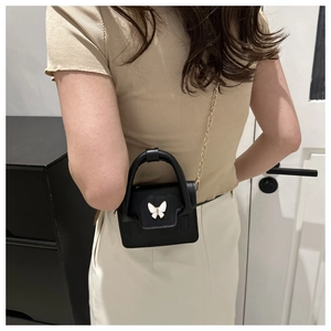 Detail view of mini black leather bag with white butterfly buckle and gold chain strap